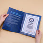 A person holding an open presentation folder displaying a GUINNESS WORLD RECORDS Certificate with a blue background, white text, and silver foil seal.