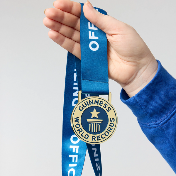 Hand holding a Guinness World Records medal with blue ribbon against a light gray background